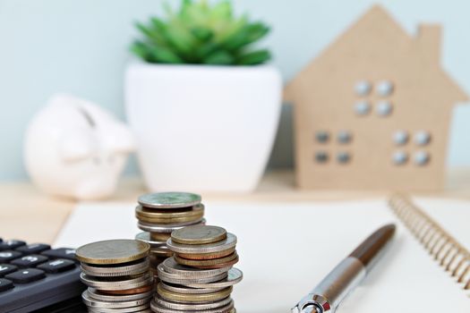 Business, finance, saving money, banking, property loan or mortgage concept : Coins stack and calculator in front of wood house model and piggy bank on office desk table