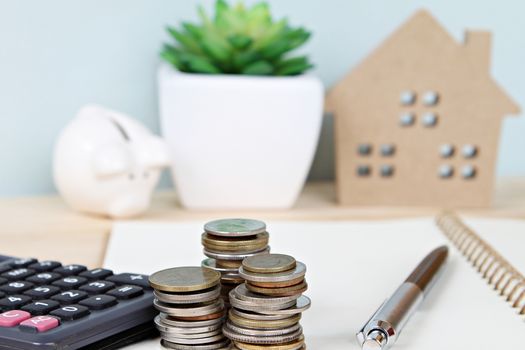 Business, finance, savings, property ladder or mortgage concept : Coins stack and calculator in front of wood house model and piggy bank