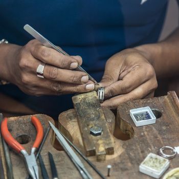 Jeweler making handmade jewelry on vintage workbench. Craft of jewelery making. Repairing ring by inlaid tight gem.