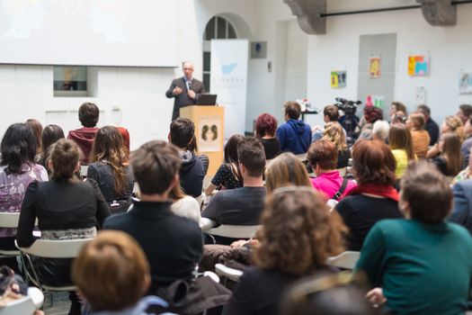 Male speaker giving presentation in lecture hall at university workshop. Audience in conference hall. Rear view of unrecognized participant in audience. Scientific conference event.