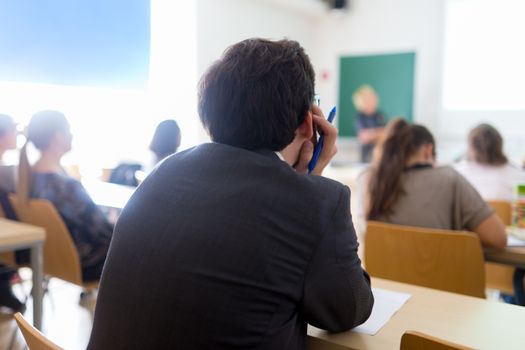 Teacher at university in front of a whiteboard screen. Students listening to lecture and making notes.