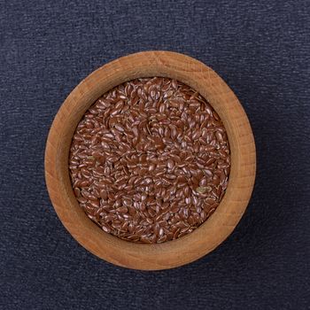 Flax seed in a wooden bowl on a black background