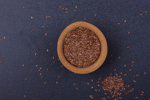 Flax seed in a wooden bowl on a black background