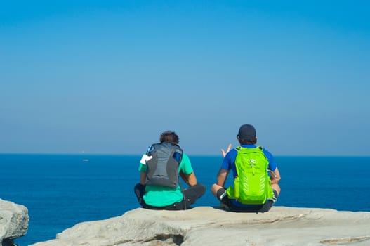 Portrait from behind of young men sitting and looking on Sea with backpack. Concept for travel or freedom.