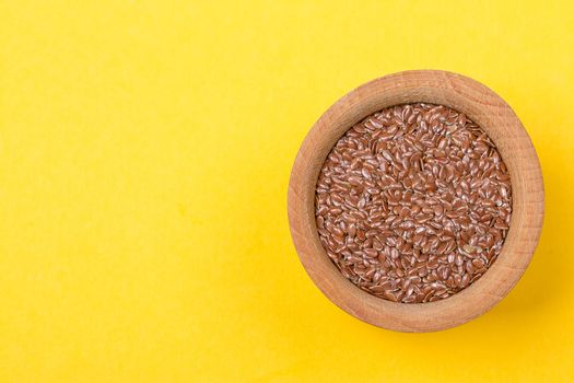 Uncooked, raw linseed or flax seed in e bowl yellow background