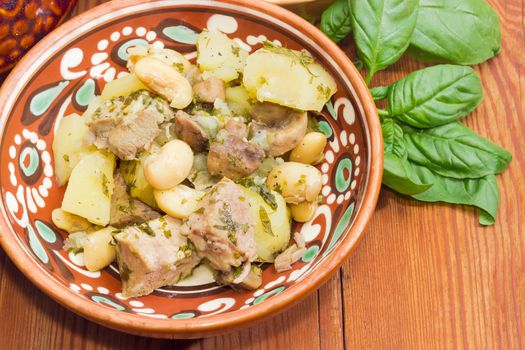 Ukrainian version of the dish Chanakhi in a clay bowl  - potatoes with meat, mushrooms and haricot beans on a surface of an old wooden planks closeup
