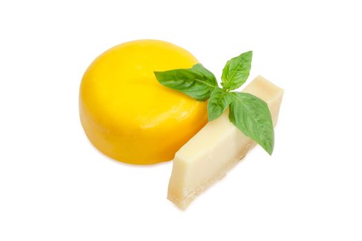 Piece of the parmesan cheese and small wheel of firm goat cheese with twig of green basil on a white background
