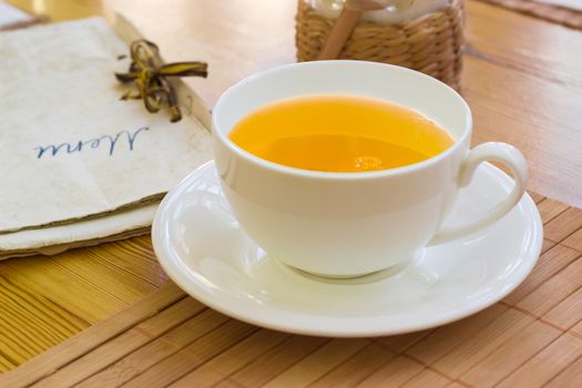 Herbal tea in the white cup with saucer on the bamboo napkin on a blurred background of a menu in retro cafe
