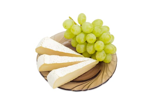 Several slices of brie cheese and cluster of the white table grapes on the dark glass saucer on a light background
