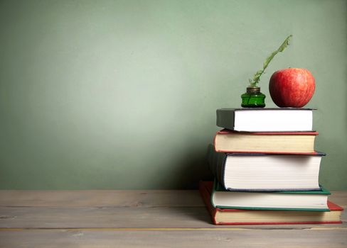 Stack of books with apple and quill next to a chalkboard background