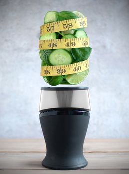 Tape measure around fresh green fruits and vegetable ingredients hovering above a blender 