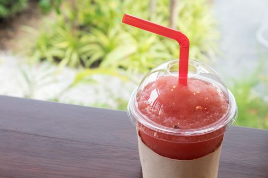 Closeup of watermelon smoothie in plastic glass on wood table, selective focus