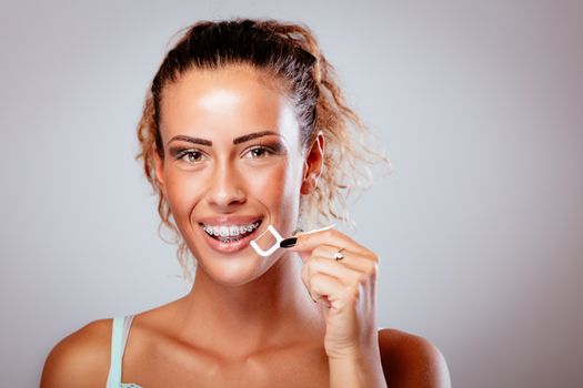 Beautiful young smiling woman with braces on white teeth and dental floss. Looking at camera.