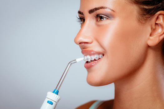 Smiling young woman with braces cleaning her teeth with oral irrigator.