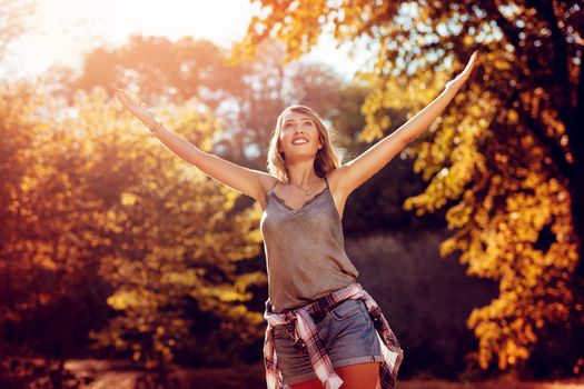 Happy young woman with open arms enjoying in the nature in autumn. 