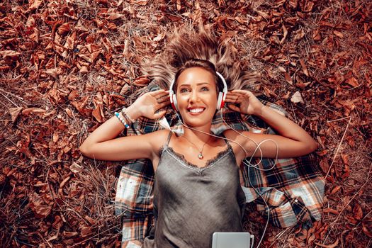 Top view of a beautiful smiling girl lying on the falls leaves and listening music.