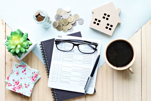 Business, finance, property ladder or mortgage loan concept : Top view or flat lay of saving account passbook or financial statement, wood house model, and coins on office desk table