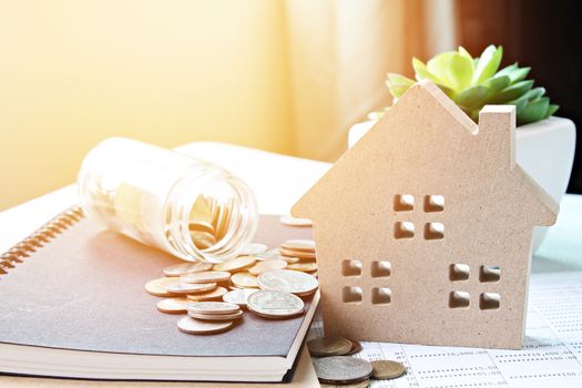 Business, finance, saving money, banking, property loan or mortgage concept :  Wood house model and coins scattered from glass jar on office desk table