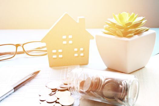 Business, finance, saving money, banking, property loan or mortgage concept :  Wood house model, saving account book or financial statement and coins scattered from glass jar on office desk table