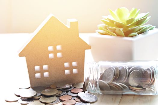 Business, finance, savings, property ladder, mortgage or loan concept : Wood house model and coins scattered from glass jar on wooden background