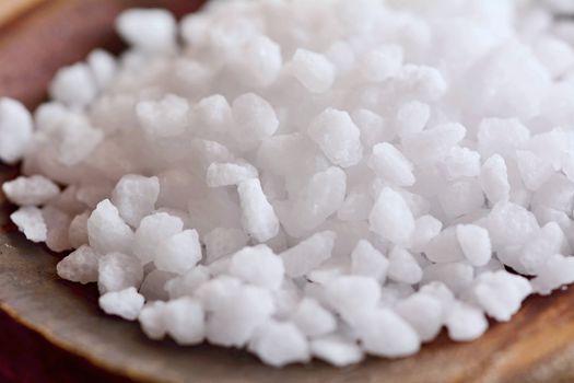 Macro shot of a white clear salt crystals on a wooden spoon.