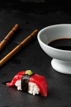  Red tuna Nigiri with Nori seaweed and wasabi paste on black slate stone with chopsticks and bowl of soy sauce. Raw fish in traditional Japanese sushi style. Vertical image.