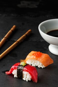  Red tuna Nigiri with Nori seaweed and wasabi paste on black slate stone with chopsticks and bowl of soy sauce. Raw fish in traditional Japanese sushi style. Vertical image.