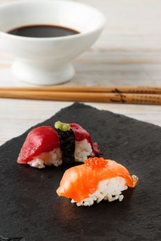 Salmon Nigiri with salmon roe on black slate stone with chopsticks and bowl of soy sauce. Raw fish in traditional Japanese sushi style. Vertical image.