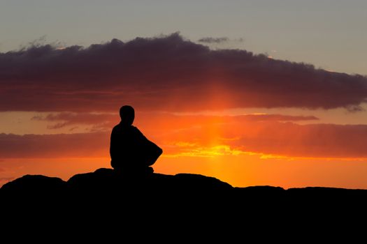 buddhist monk meditating at sunset sitting on a rock by the sea