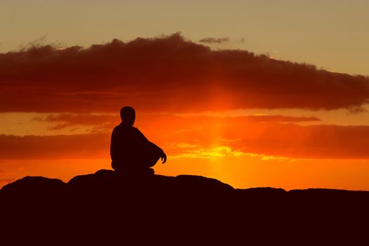 buddhist monk meditating at sunset sitting on a rock by the sea