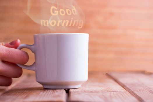 White cup on blue wooden table. Text GOOD MORNING on background