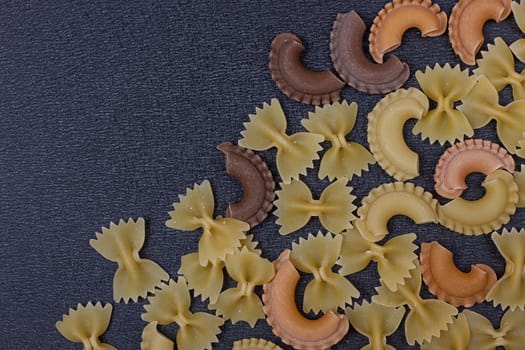 Variety of types of Italian pasta background. Set of raw dry pasta on a black slate background.