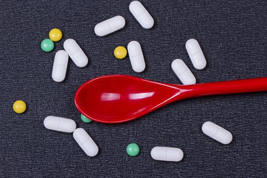 Assorted pharmaceutical medicine pills, tablets and capsules on wooden spoon. black background