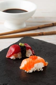 Salmon Nigiri with salmon roe on black slate stone with chopsticks and bowl of soy sauce. Raw fish in traditional Japanese sushi style. Vertical image.