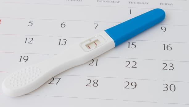 Pregnancy test on calendar background, health care concept