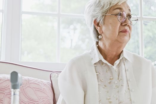 senior woman portrait, senior woman sitting alone on a sofa at home in a lonely mood.