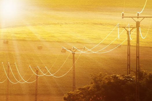 beautiful sunlight over the fields, electricity lines in foreground, orange colors of sunset