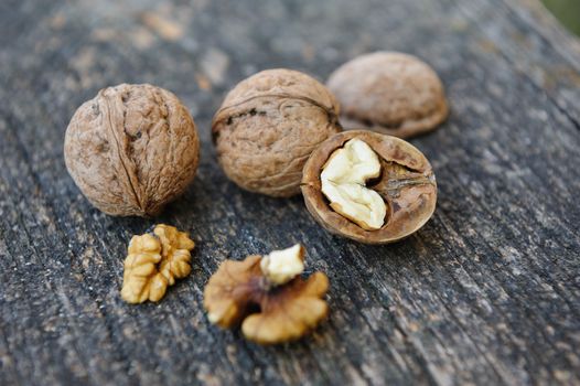 Whole and cracked walnuts at old wooden plank. Still life with selective focus.