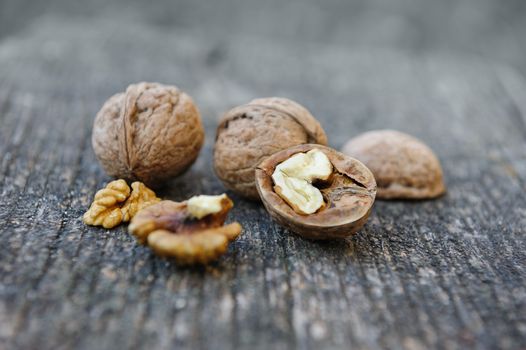 Whole and cracked walnuts at old wooden plank. Still life with selective focus.