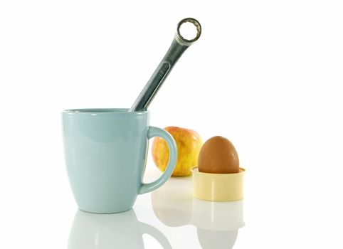 time for a coffee break during work with blue coffe cup and metal boxwrench or spanner with apple and egg as background  isolated on white