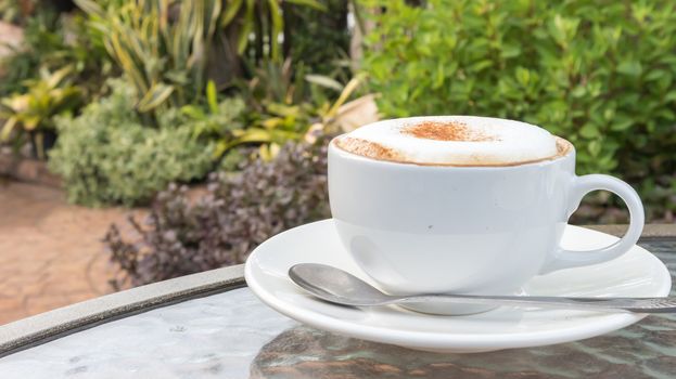 Closeup A cup of hot cappuccino on glass table with garden nature background