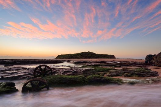 Sunrise skies with pretty wispy cloud over Windang Island with old abandoned train wheels in the foreground ocean flows.