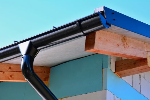 Closeup of a black steel roof rain gutter on a new house with insulated wall.