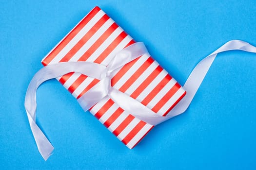 Gift in red and white packing with ribbon on a blue background. a Christmas gift