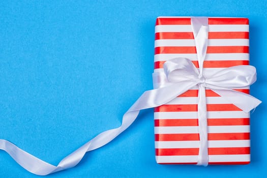 Gift in red and white packing with ribbon on a blue background. a Christmas gift