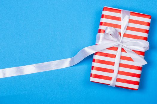 Gift in red and white packing with ribbon on a blue background. a Christmas gift