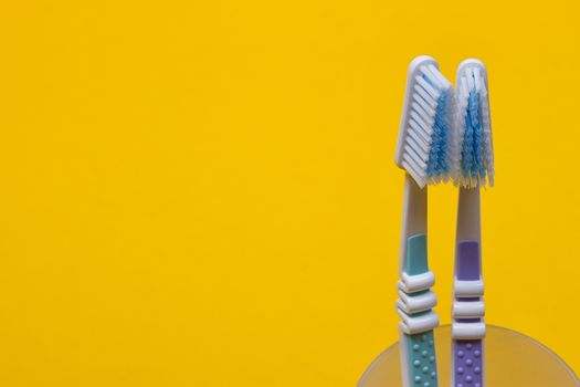 two toothbrushes in a glass on the yellow background. Top view