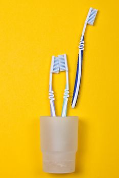 three toothbrushes in a glass on the yellow background. Top view