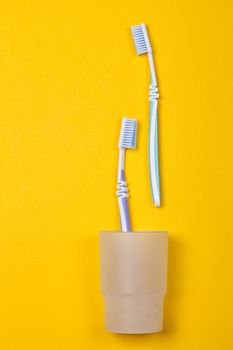 two toothbrushes in a glass on the yellow background. Top view