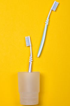 two toothbrushes in a glass on the yellow background. Top view